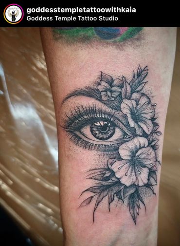 Very detailed black and grey human eye and flowers in a style that blends realism and illustrative