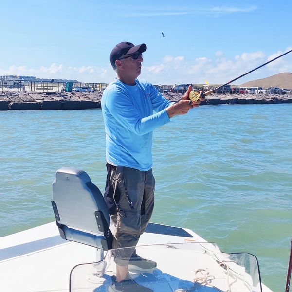 Man fishing on a boat under clear blue skies.