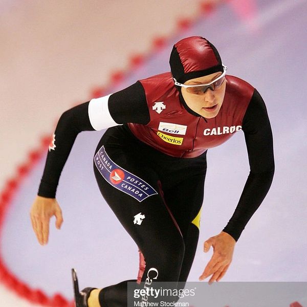 Speed skater in action wearing a maroon and black suit on ice rink.