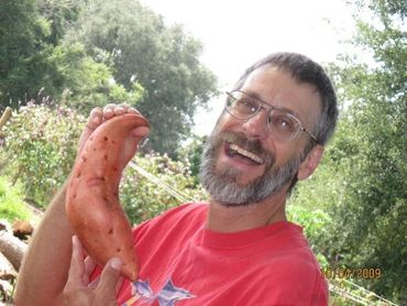 Man smiling and holding a large sweet potato outdoors.