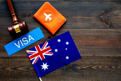 Gavel, visa card, Australian flag, and orange passport on wooden table.