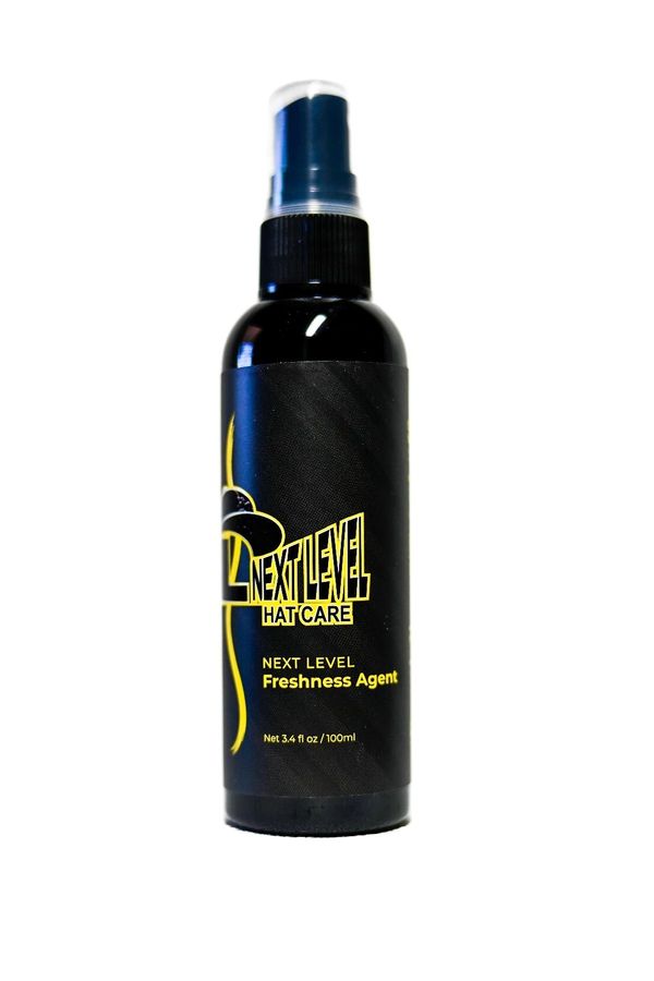 A black spray bottle labeled Next Level Hat Care Freshness Agent.