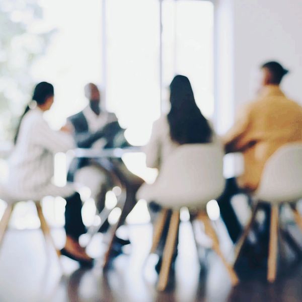 A blurred group of business people meeting around a table in front of large windows.
