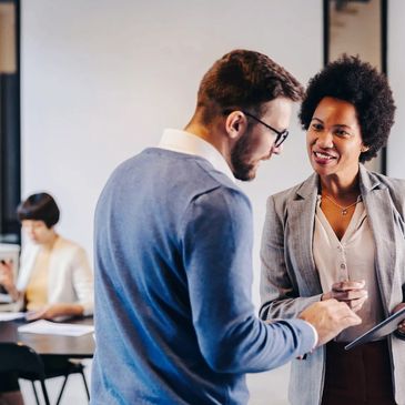 Two people in a stand-up meeting with a woman working behind them.