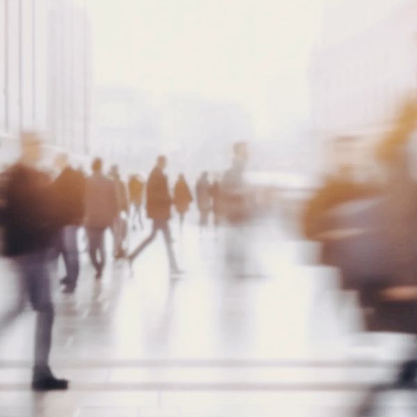 A blurred image of people walking on a city street in professional attire.