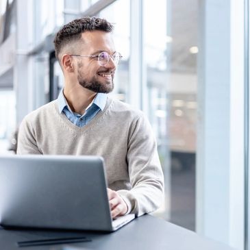 A man with his head turned smiling at something while his hands rest on a laptop.
