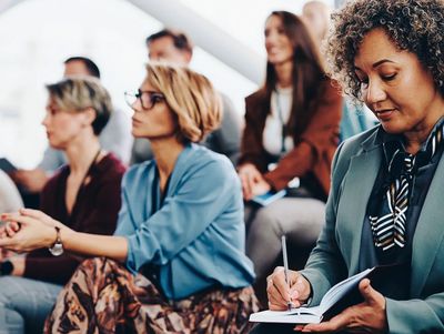 A group of people attending training with a woman taking notes in the front row.