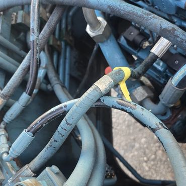 Close-up of worn and cracked blue hydraulic hoses and metal fittings.