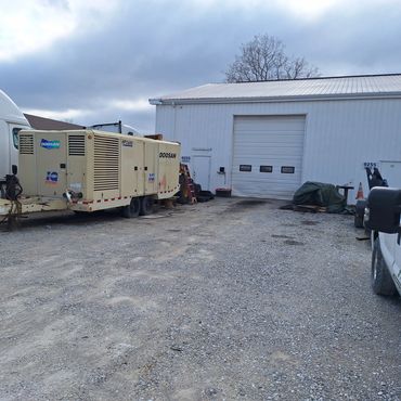 Industrial yard with trucks, equipment, and a white building under a cloudy sky.