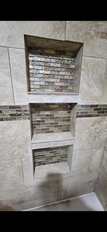 Three recessed shelves with mosaic tile backs in a beige tiled shower.