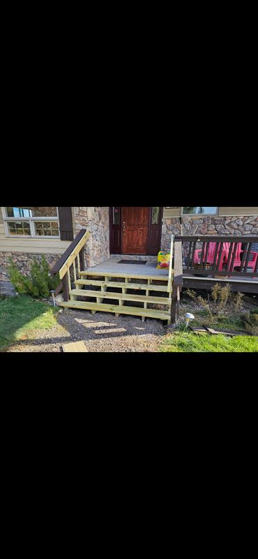 Newly built wooden stairs leading to a front door with stone siding.