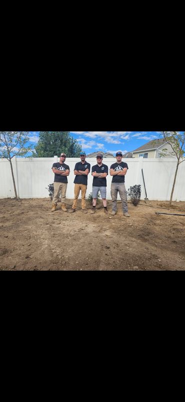 Four men standing with arms crossed in a dirt backyard.