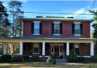 A two-story brick house with black shutters and Christmas wreaths on the porch.