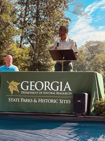 A man speaks at a Georgia State Parks & Historic Sites event outdoors.