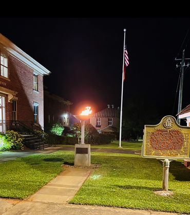 A nighttime scene with a burning flame monument, flagpole, and historical marker in Wilkinson County.