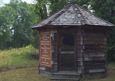 Historic wooden convenience store with a shingled roof in a rural setting.