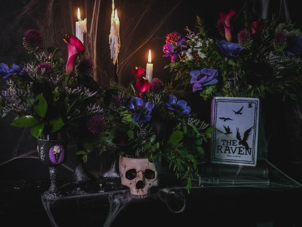 Gothic floral arrangement with purple flowers, candles, and Edgar Allan Poe-inspired details.