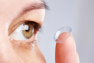 Person holding a contact lens on fingertip near the eye.