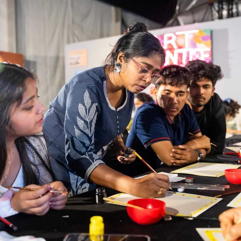 A woman teaches painting to a group of attentive young adults.