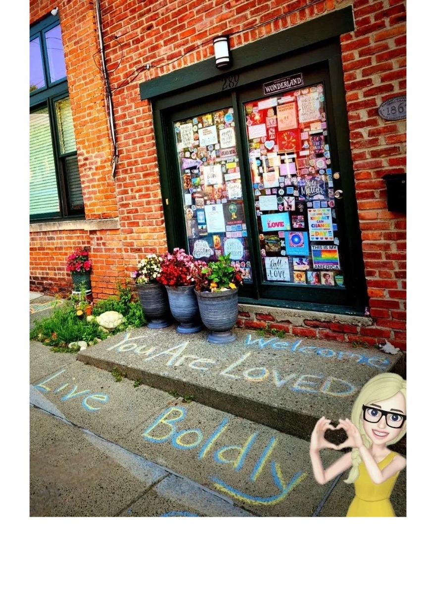 Colorful chalk message says "You Are Loved, Live Boldly" outside a brick building with flower pots.