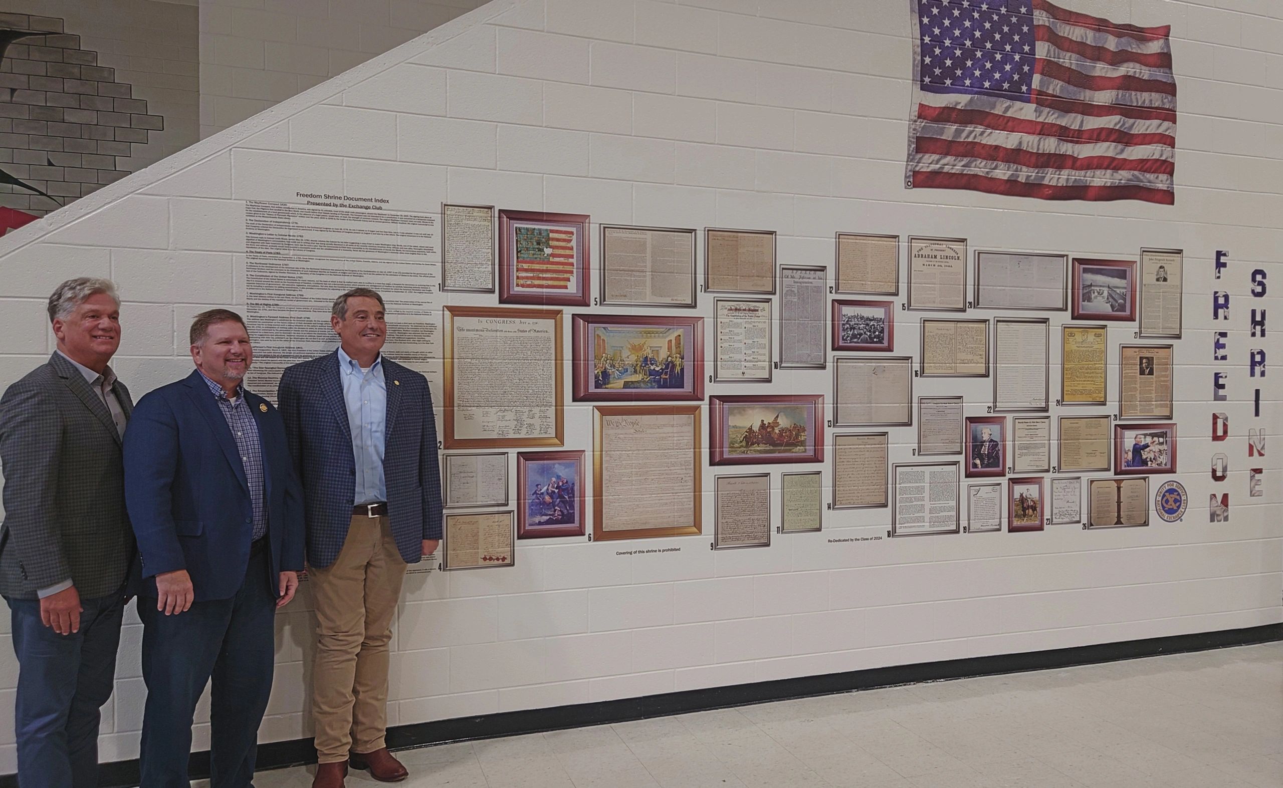 Three men standing beside a Freedom Shrine display with historic documents and an American flag, printed by our robot