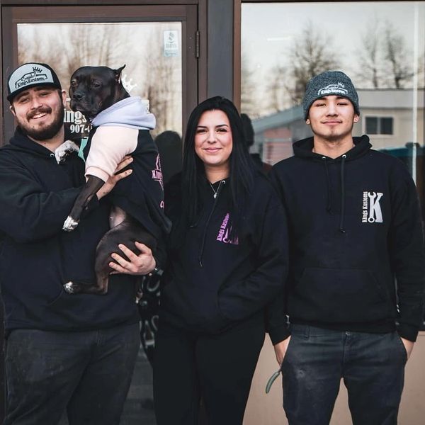 Three people and a dog smiling in matching hoodies outside a building.