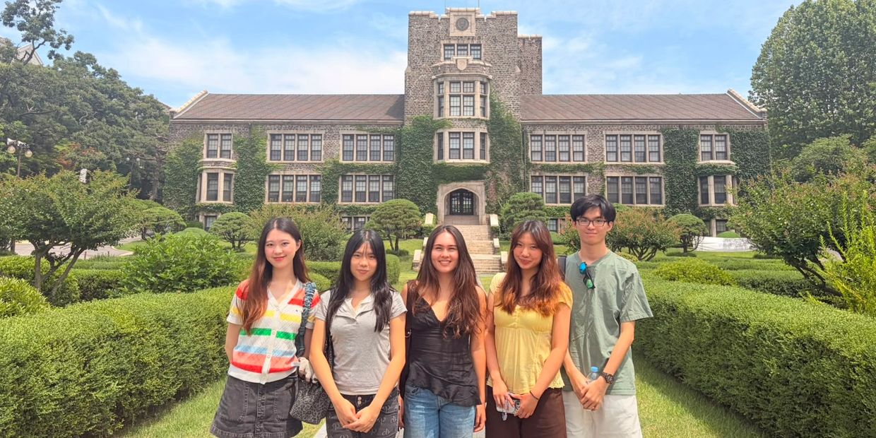 Group of five young adults posing in front of a historic ivy-covered building.