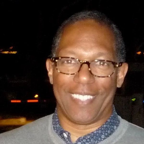 Dr. Laurie from Positive Psychology Inc.,  a man smiling with brown glasses and a gray sweater.