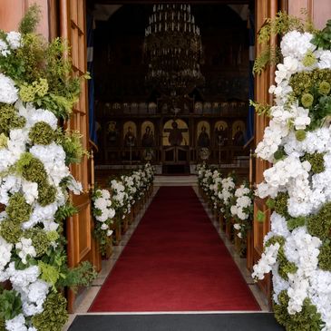 Church entrance decorated with white flowers and red carpet.