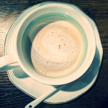 A cup of frothy coffee on a saucer with a spoon on a wooden table.