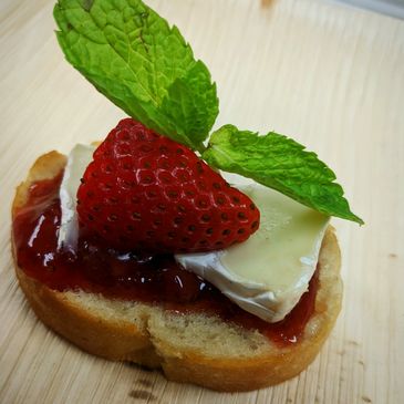 Appetizer with strawberry, cheese, jam, and mint on bread.