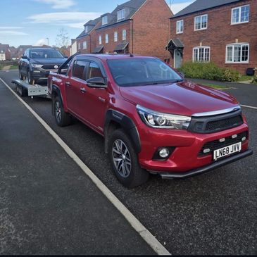 Red pickup truck towing a black Volkswagen SUV on a trailer in a residential area.