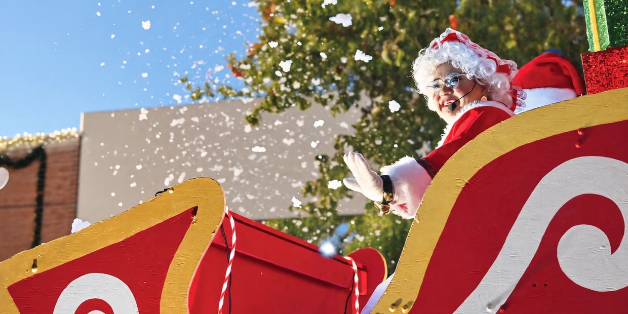 Mrs. Claus waving from a festive sleigh with snowflakes.
