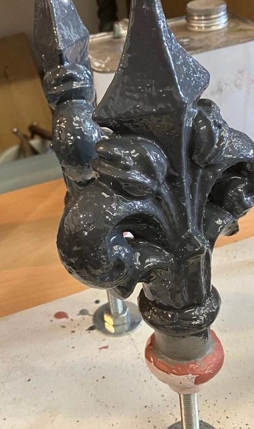 Glossy black ornamental finials with fleur-de-lis design on a workbench.