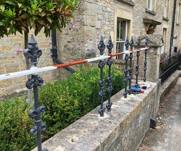 Iron fence spindles being painted white and red on a stone wall.