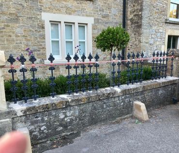 Black wrought iron fence with pink horizontal bars in front of a stone building.