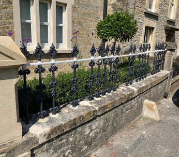 Ornate black iron fence on a stone wall in front of a stone building.