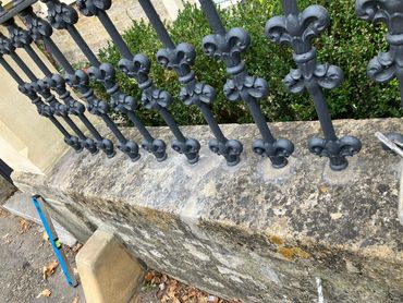 Black wrought iron fence with fleur-de-lis design on a stone wall.