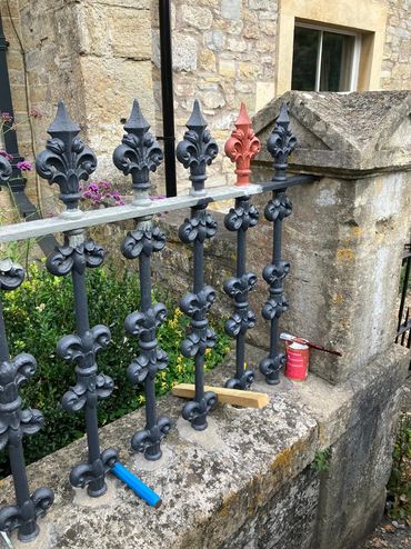 A black iron fence with one red-painted spike and painting supplies nearby.