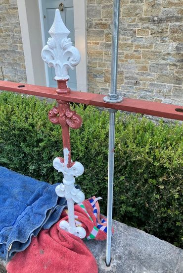 Partially painted ornate iron fence post with towels underneath.