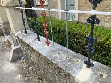 Old stone wall with metal railings being repaired and reinforced.