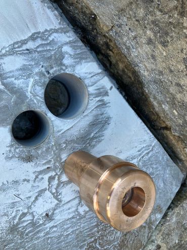 Close-up of a bronze or brass fitting on a carved stone surface with two round holes.
