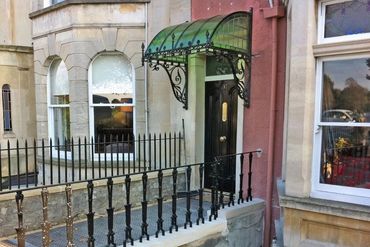 Black iron gate and green canopy above a black door in a stone building.
