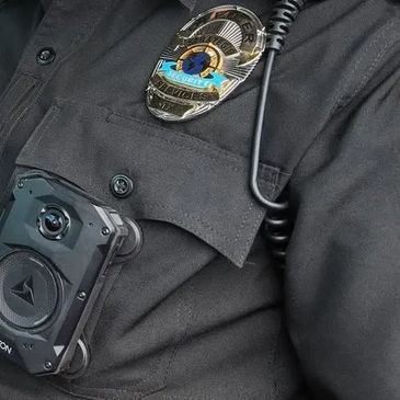 Close-up of a security officer's uniform with a body camera and badge.