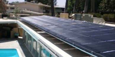 Solar panels installed on a rooftop next to a swimming pool under clear skies.