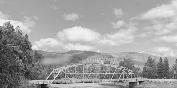 Metal truss bridge over a river in a natural setting.