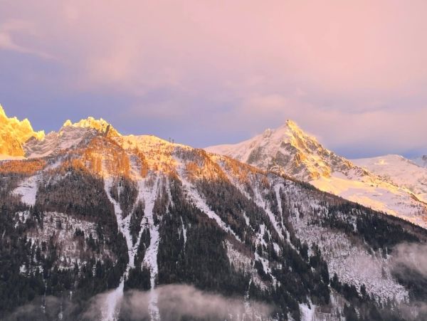 Snowy mountain peaks at sunset with pink sky.