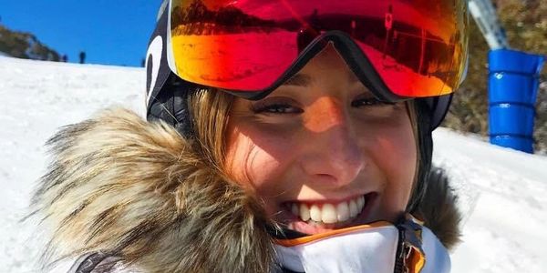 Smiling person in ski gear with reflective goggles.