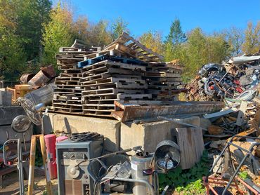 Stacked wooden pallets and scrap metal in an outdoor junkyard on a sunny day.