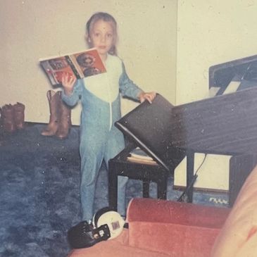 Young child holding a book near a piano in a cozy room.
